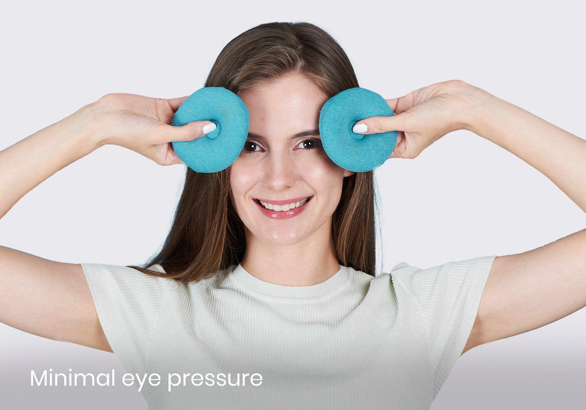 Smiling woman holding blue Manta COOL eye cups over her eyes against grey background with text "Minimal eye pressure".